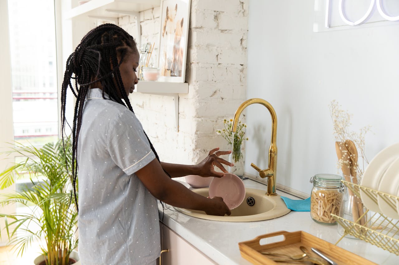 About An adult woman washing dishes in a bright, modern kitchen setting.