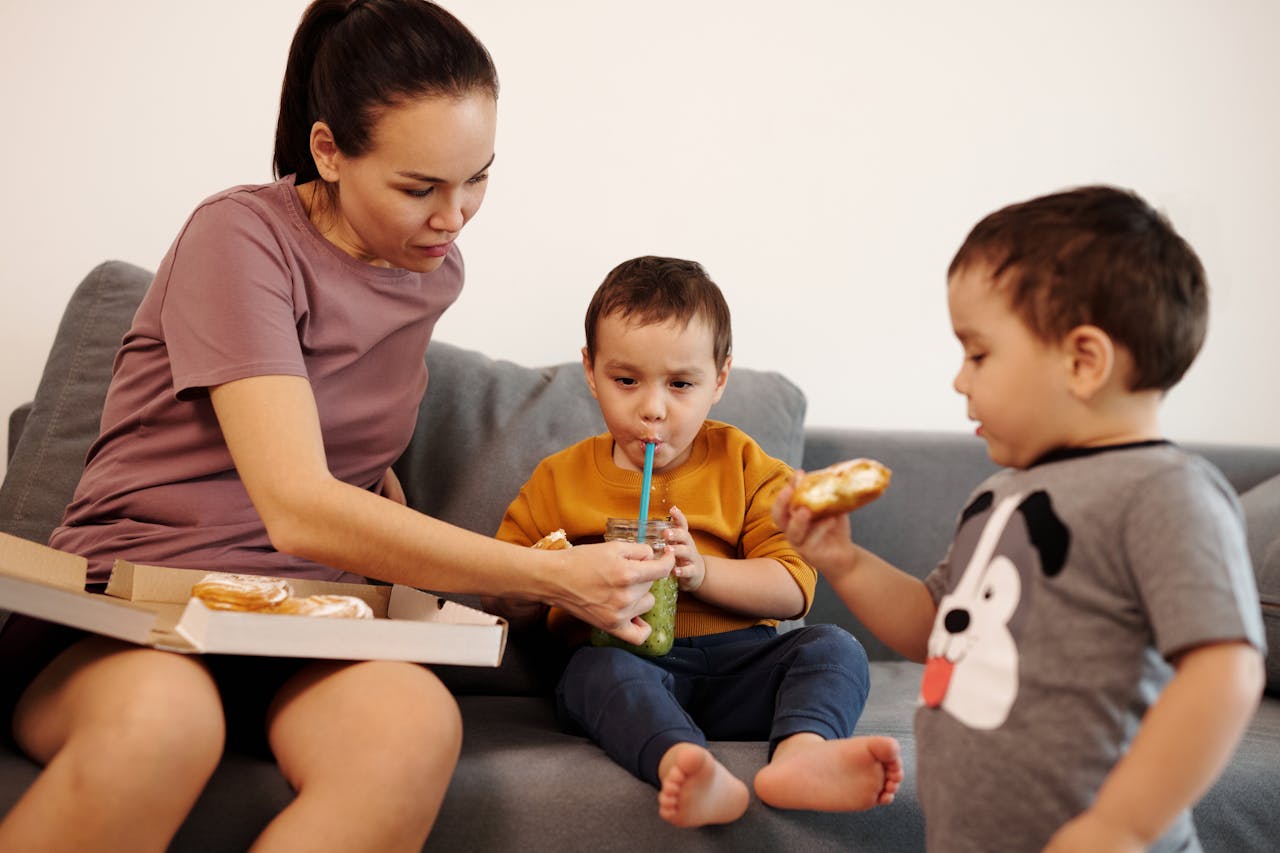 Home A mother and her twin boys share a snack on a cozy couch, highlighting family bonding.
