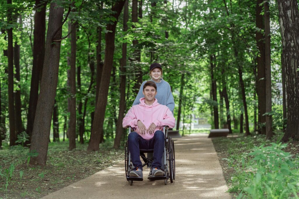 pexels photo 8415822 8415822 Smiling couple enjoying a sunny day in a park. Man in a wheelchair being pushed by a woman.